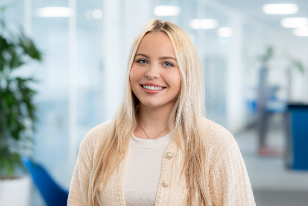 Portrait Jaclyn Schikora. Frau lächelt in einem Büro mit Pflanzen und moderner Einrichtung. Portrait Jaclyn Schikora. Frau lächelt in einem Büro mit Pflanzen und moderner Einrichtung.