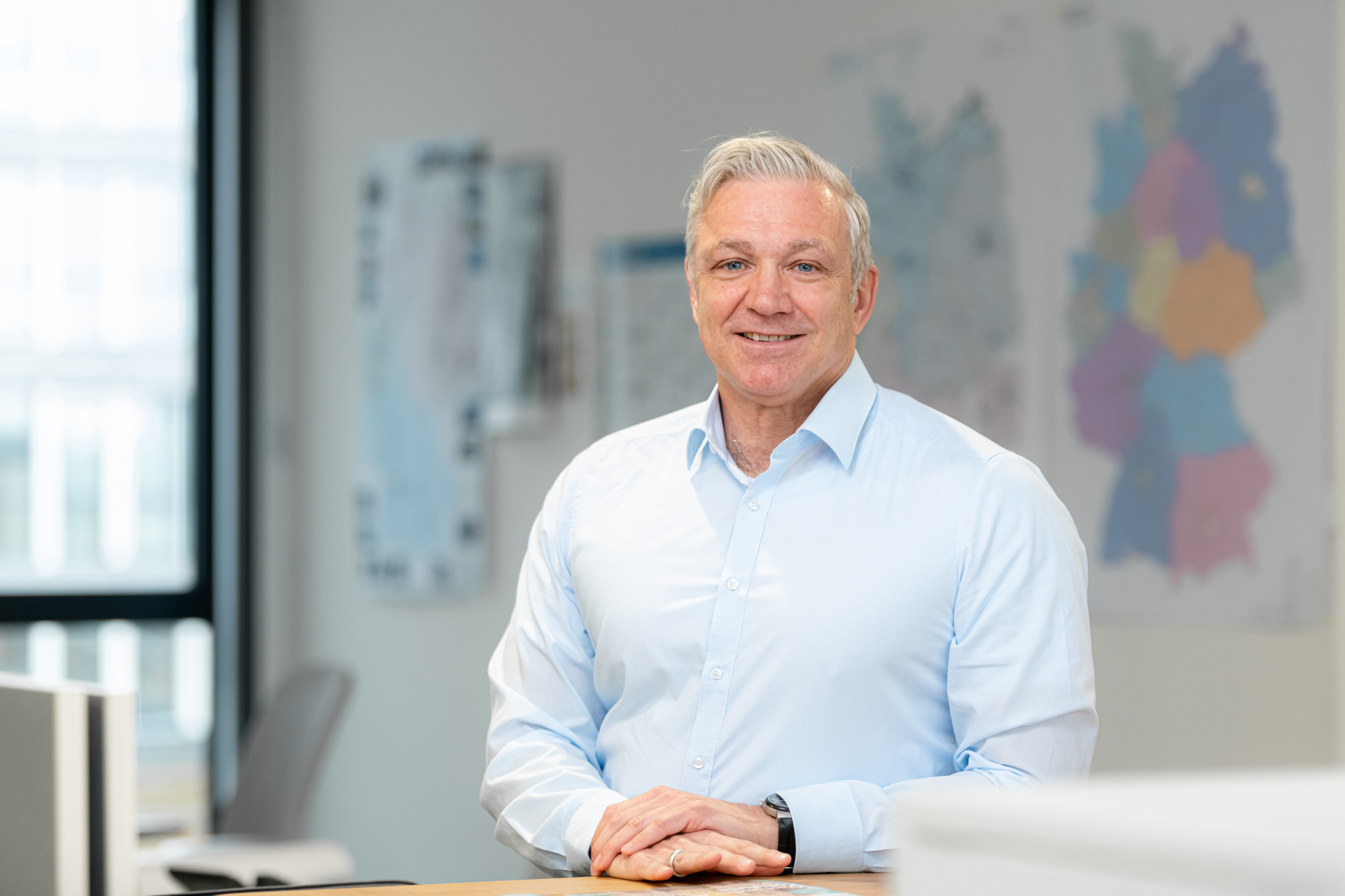 Portrait Norbert Rieger. Mann in hellblauen Hemd, Hände auf einem Tisch gelegt, unscharfer Raum im Hintergrund. Portrait Norbert Rieger. Mann in hellblauen Hemd, Hände auf einem Tisch gelegt, unscharfer Raum im Hintergrund.