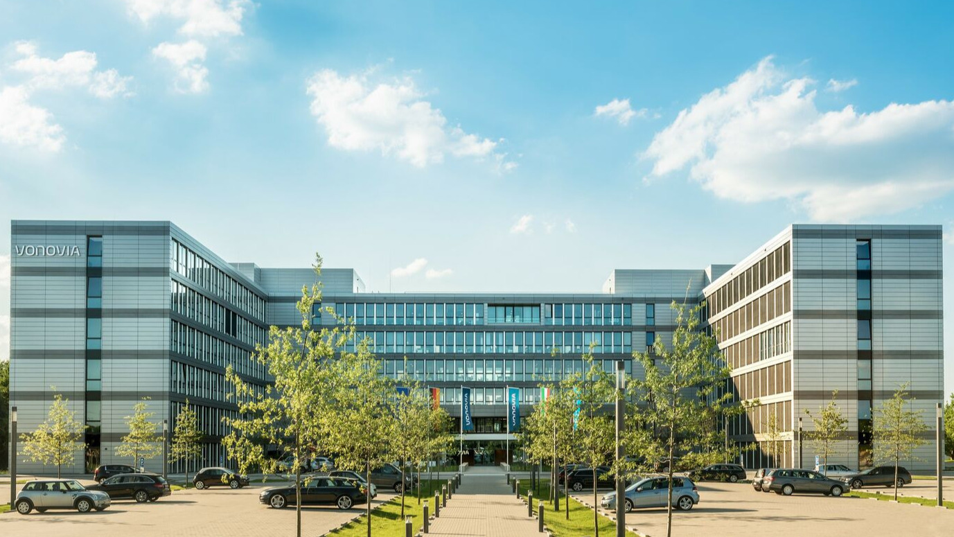Großes, modernes Gebäude mit Vonovia Schriftzug, Autos im Vordergrund, leicht bewölkter Himmel Großes, modernes Gebäude mit Vonovia Schriftzug, Autos im Vordergrund, leicht bewölkter Himmel